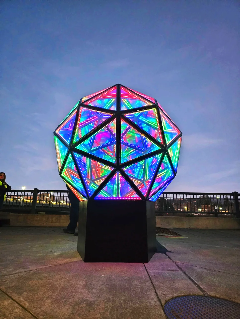 The Infinity Temple’s geometric mirrored panels glowing with multicolored LED lights at dusk.