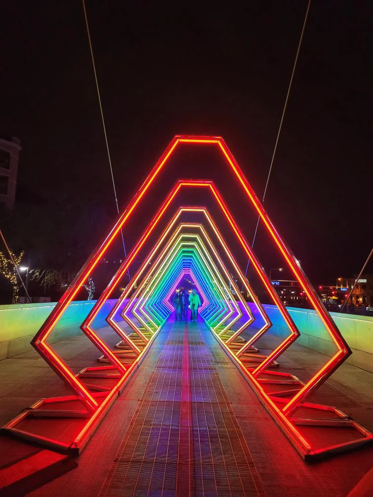 Visitors walking through The Tunnel’s repeating geometric arches of rainbow-colored light.